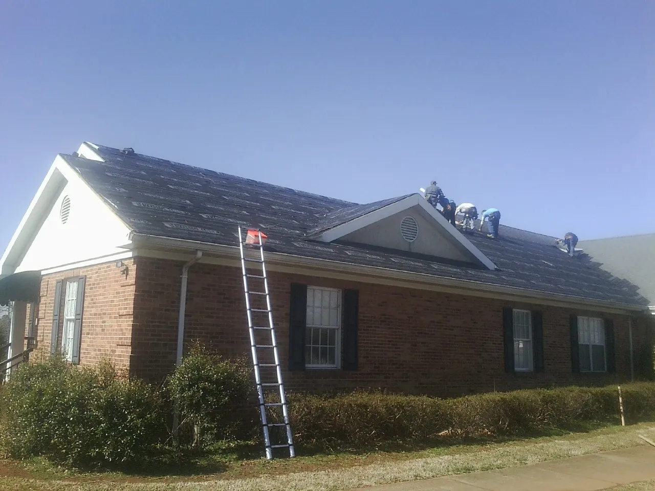 Crew tearing shingles off a brick ranch roof with a ladder set — Metal Roof Repair work by our crew in Loma Linda
