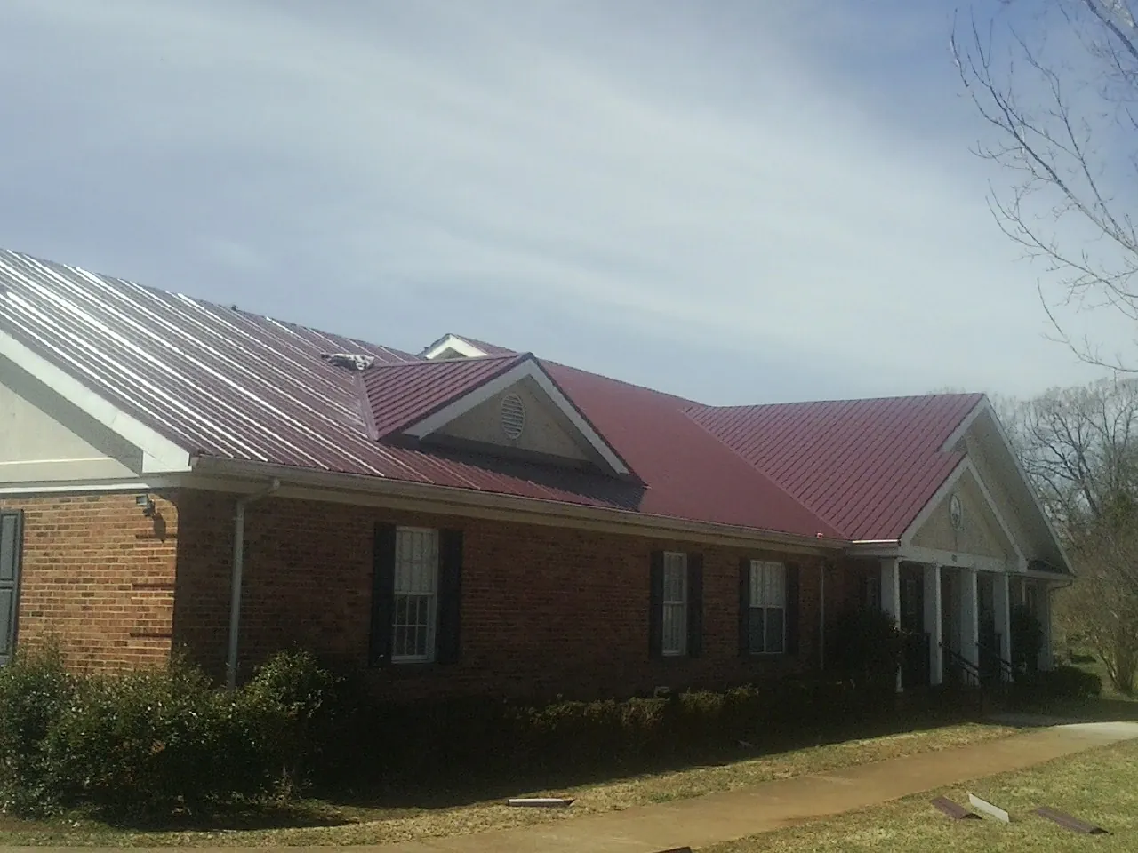 Red metal roof with gabled entries on a long brick building, from a Hail Damage Roof Repair job in Loma Linda