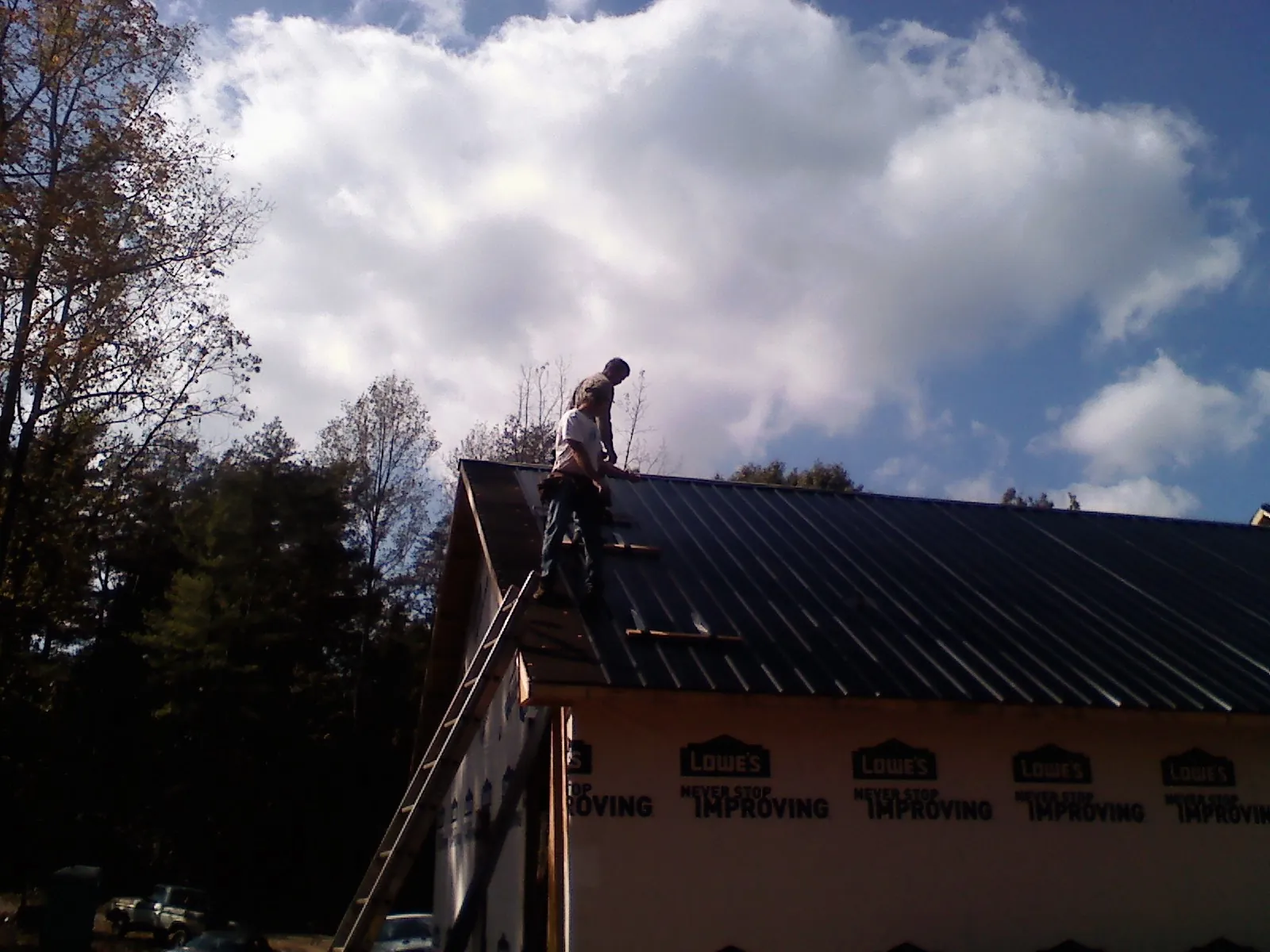 Roofer fastening dark metal panels high against a cloudy sky, from a Roof Inspection job in Loma Linda