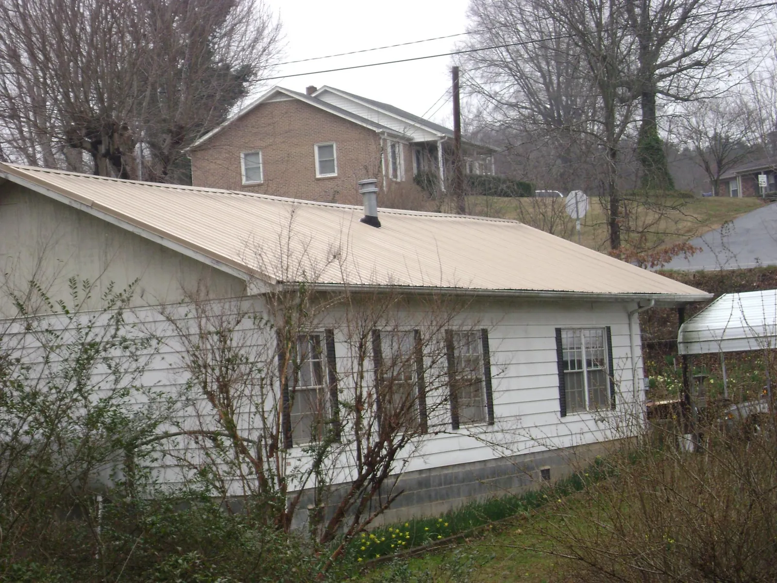 Tan metal roof on a white sided house set into a hillside — Commercial Roofing by Roofing Brothers in Loma Linda